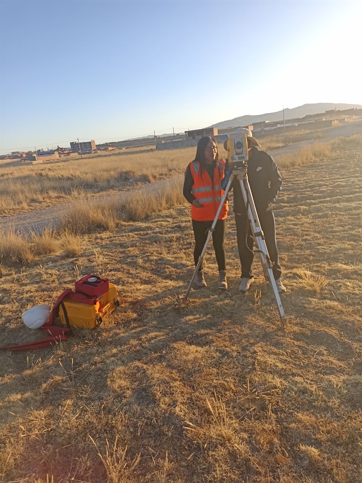 Levantamiento topográfico con trípode en una pampa altoandina, con dos integrantes del equipo con chaleco.