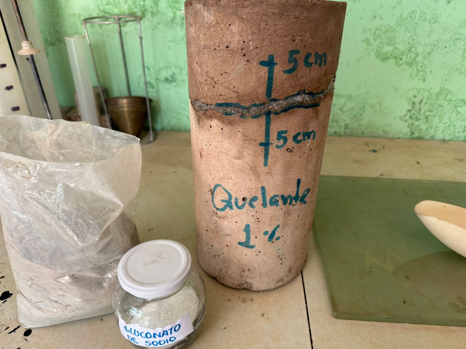 Probeta de concreto rotulada Quelante 1 % junto a un frasco de gluconato de sodio, en el laboratorio.