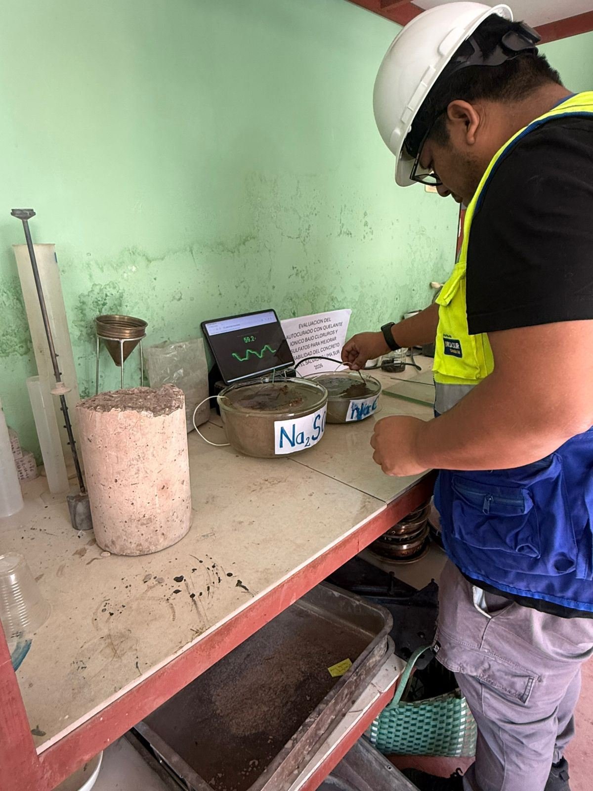 Ingeniero con casco registra la lectura de un ensayo de durabilidad del concreto con sulfatos y cloruros en el laboratorio.